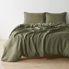 an unmade bed with green sheets and pillow cases on top of it in a white room