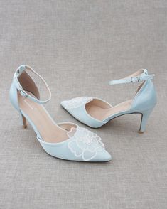 a pair of blue high heels with white flowers on the heel and ankle strap, sitting on a gray surface