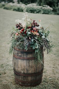 a wooden barrel with flowers and greenery in it sitting on the side of a field