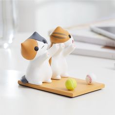 two cat figurines on a cutting board with a ball in the foreground