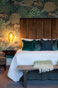 a bed with green and white pillows in a bedroom next to a wallpapered wall