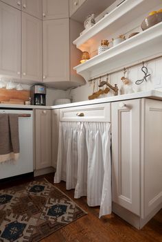 a kitchen with white cupboards and cabinets has an area rug on the hardwood floor