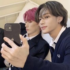 two young men sitting next to each other while looking at a cell phone screen in front of them