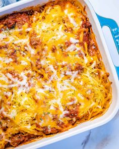 a casserole dish with meat and cheese in it on a blue towel next to a fork