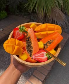 a person holding a wooden bowl filled with fruit and veggies on top of it