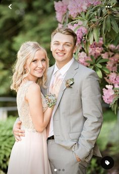 a man and woman standing next to each other in front of pink flowers on a tree