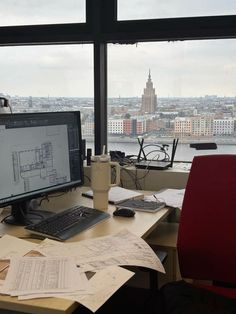 a desk with a computer monitor, keyboard and mouse in front of a large window