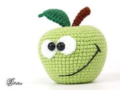 a crocheted green apple with eyes and a leaf on it's side