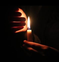 a person holding a lit candle in their hand with the light shining on it's face