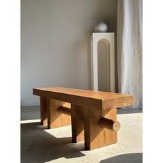 a wooden bench sitting on top of a cement floor next to a tall white vase