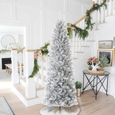 a decorated christmas tree in the middle of a room with stairs and pictures on the wall