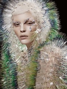 a woman with white hair and silver make - up on her face is surrounded by feathers