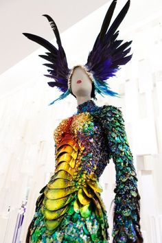 a dress made out of different colored material with wings on the head and shoulders, in front of a white wall