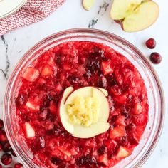 cranberry sauce in a glass bowl with an apple on top and other fruit around it