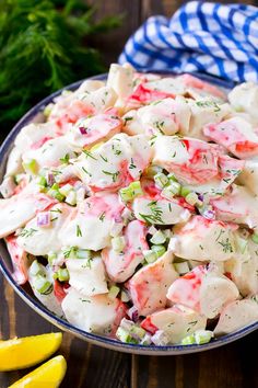 a bowl full of crab salad with lemons and dill in the background on a wooden table