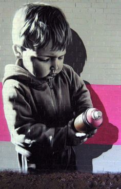 a young boy is holding a bottle in front of a wall with a painting on it