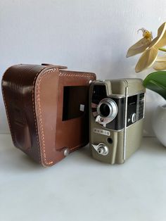 two old cameras sitting next to each other on a white table with flowers in the background