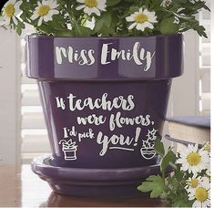 a purple flower pot sitting on top of a wooden table next to white daisies