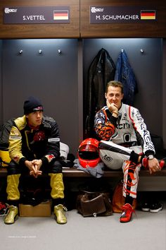 two men sitting on a bench in a locker room with helmets and jackets around them