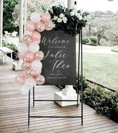 a welcome sign with pink and white balloons in front of it on a wooden deck