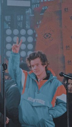 a man giving the peace sign while standing in front of microphones with his hand up