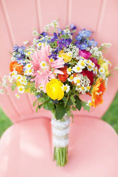 a bouquet of colorful flowers sitting on top of a pink chair in front of grass