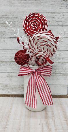 a white vase filled with red and white lollipops on top of a wooden table