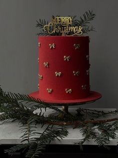 a red and gold christmas cake with pine branches on the top, decorated with merry christmas decorations