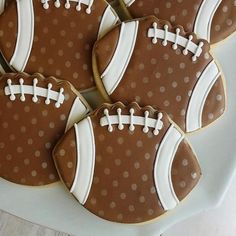 four decorated cookies in the shape of footballs on a white platter with polka dots