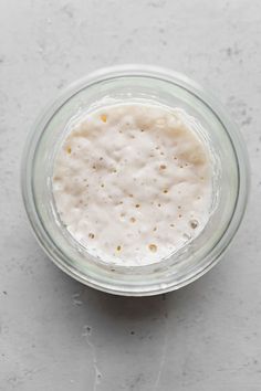 a glass bowl filled with white liquid on top of a gray counter next to a spoon