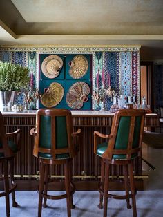 a bar with green leather chairs and plates on the wall above it, along with two vases filled with flowers