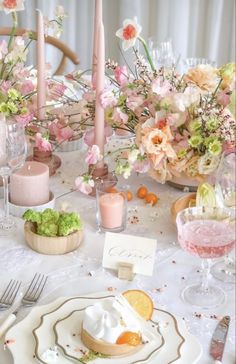 the table is set with pink and white flowers, silverware, candles, and napkins