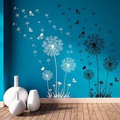 a blue wall with dandelions and butterflies in the air next to two vases