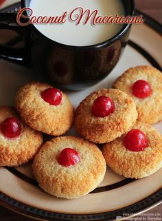 small cookies with cherries are on a plate next to a cup of milk