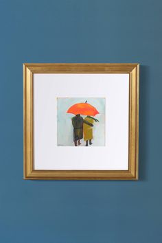 two people standing under an orange umbrella in front of a blue wall with a gold frame