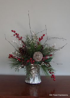 a silver vase filled with red berries and greenery on top of a wooden table