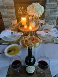 two glasses of wine and bread on a table next to a bottle of red wine