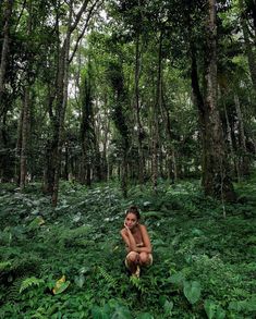 a woman kneeling in the middle of a lush green forest