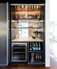 a bar with wine glasses and bottles on the shelves next to an open refrigerator door