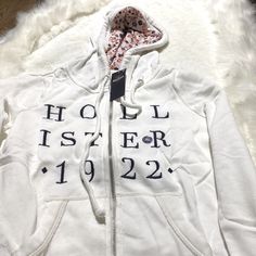 White Zip Up Hoodie By Hollister. Shop Now. White Cotton Hooded Jacket For Fall, Cozy Winter Outerwear With Letter Print, White Sweatshirt For Cold Weather In Fall, White Sweatshirt For Fall, Hooded Cotton Tops For Cold Weather, Fitted White Hoodie For Winter, Trendy White Cotton Hooded Jacket, Cotton Hooded Top For Cold Weather, Cozy White Hooded Jacket For Fall