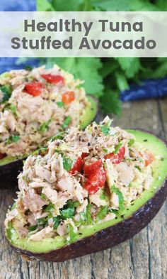 an avocado filled with tuna salad on top of a wooden table next to other food