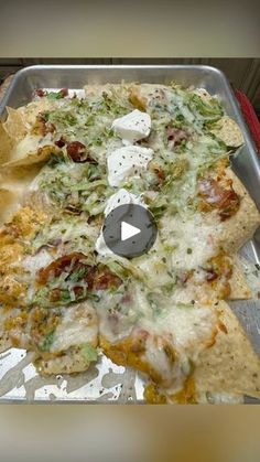 a metal pan filled with pizza covered in cheese and veggies next to tortilla chips