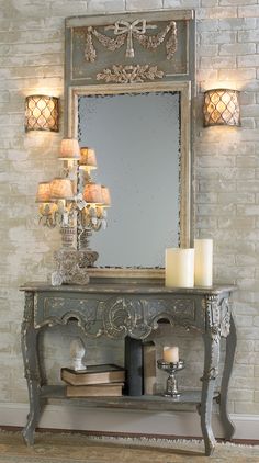 a mirror and some candles on a table in front of a brick wall with a chandelier