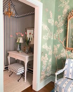 a chair and table in a room with wallpaper on the walls, mirror above it