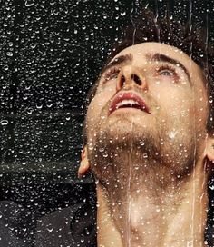 a man is looking up at the sky through a rain soaked window with drops of water on it