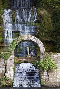 a man is standing at the end of a bridge over a river with a waterfall in the background