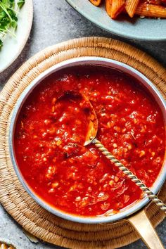 a bowl of pasta sauce with a spoon in it on a wooden tray next to other dishes