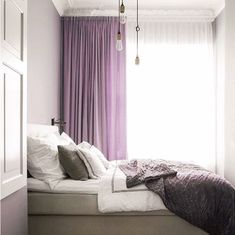 a bed sitting under a window next to a purple curtain