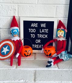 two elfs sitting next to each other on a brick wall with a sign that says are we too late to trick or treat