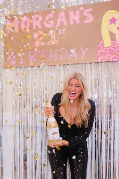 a woman holding a champagne bottle and confetti in front of a birthday sign